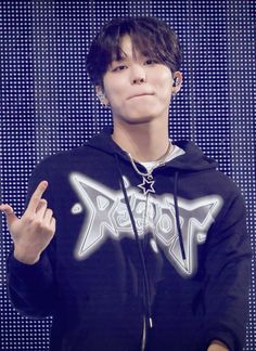 a young man in a black hoodie holding his hand up to the side and making a peace sign