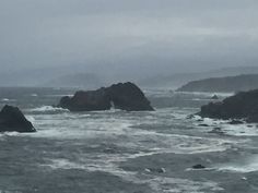 the ocean is choppy and stormy with rocks in the foreground on an overcast day