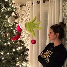 a woman standing in front of a christmas tree with the grin face on it's head