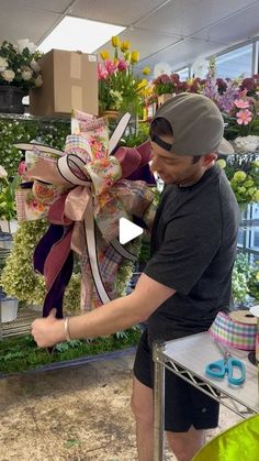 a man holding a large bow in front of a flower shop display filled with lots of flowers