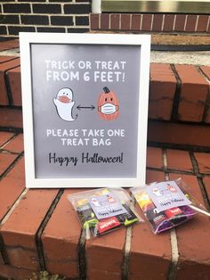 a trick or treat from 6 feet sign next to two bags of candy on the ground