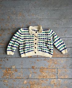 a white and blue sweater sitting on top of a wooden floor next to a wall