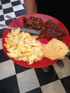 a red plate topped with pasta, meat and veggies on top of a checkered table