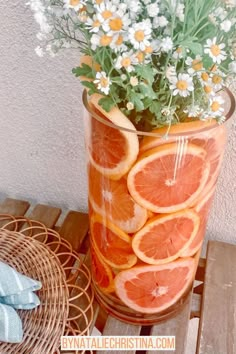 a vase filled with oranges and daisies sitting on top of a wooden table