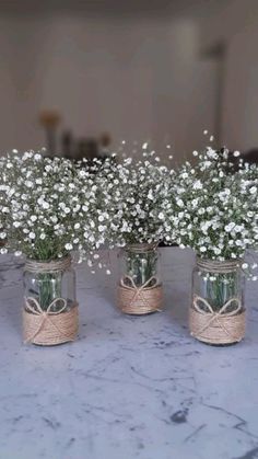 three mason jars with baby's breath flowers tied in twine on a table