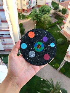 a hand holding up a piece of paper with planets on it in front of a cityscape