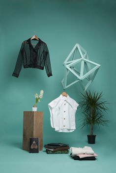 clothes hanging on a clothes rack next to a potted plant and a paper bag