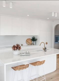 a white kitchen with two stools next to the counter top and an island in front of it