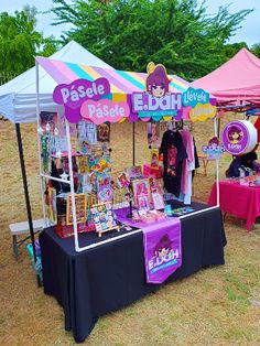 an outdoor vendor stall with posters and other items for sale on the grass under umbrellas