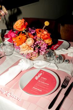 the table is set with pink and orange flowers, silverware, and napkins