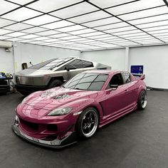 two cars parked in a garage next to each other, one is pink and the other is black