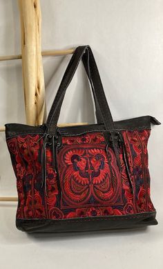 Pranee Phoenix Collection Sierra in Black      #100-G Sierra, from the Phoenix Collection, is a soft black leather tote with hand-sewn embroidery (front to back) in a bold mythical design paired with a bold color palette: red, blue, and purple to name a few. Pranee Handcrafted Unique Designer Bags are beautiful artisan-made bags completely handmade using genuine leather, hand sewn embroidery, and unique decorative stitching.  There is an incredible amount of care and attention to details taken in the craftsmanship of every Pranee bag.  Each piece is made with genuine leather, hemp or cotton, and unique hand-sewn embroidery and/or applique. Features *        Zipper closure *        Interior side pockets and zipper pocket *        Genuine leather handle and accents  Specifications *        D Black Embroidered Double Handle Shoulder Bag, Embroidered Black Shoulder Bag With Double Handle, Black Embroidered Double Handle Bag, Black Embroidered Tote Shoulder Bag, Embroidered Black Shoulder Bag For Travel, Traditional Black Shoulder Bag With Leather Handles, Embroidered Leather Shopping Bag, Leather Double Handle Embroidered Bag, Hand-stitched Travel Bags