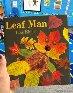 a person holding up a leaf man book in front of a table with other books on it