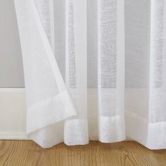 a cat sitting on top of a wooden floor next to a window covered in white curtains