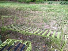 a green metal bed frame sitting on top of a grass covered field next to a trash can