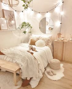 a bedroom with white walls and wooden flooring is lit by fairy lights, while a bed sits in front of a mirror on the wall