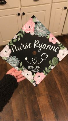 a black and white floral graduation cap with the name nurse ryane on it in front of cabinets