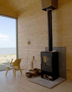 a living room with a wood burning stove in the center and large windows overlooking the ocean