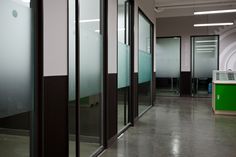 an office hallway with glass doors and green desks in the center, along with other cubicles