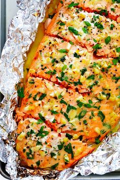 salmon fillets in foil with herbs and seasoning on top, ready to be cooked