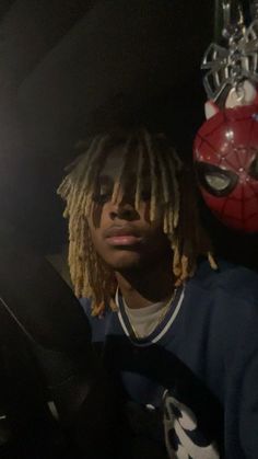 a man with dreadlocks sitting in the back seat of a car next to a spiderman mask