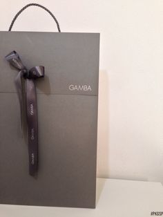 a gray gift bag with a black ribbon on it and the word gamba written in white