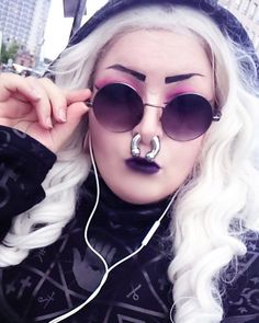 a woman with white hair wearing sunglasses and a hoodie is listening to headphones