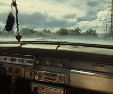 the dashboard of an old car with clouds in the sky and trees on the other side