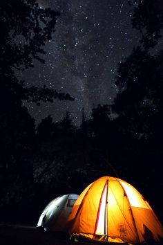 two tents are lit up at night with the stars in the sky above them and trees