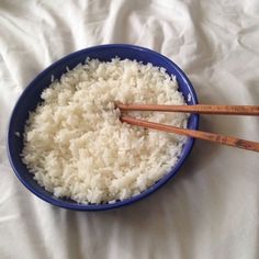 rice and chopsticks in a blue bowl on a white sheet with a wooden spoon