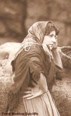 an old photo of a woman leaning on a rock talking on her cell phone while holding a basket behind her head