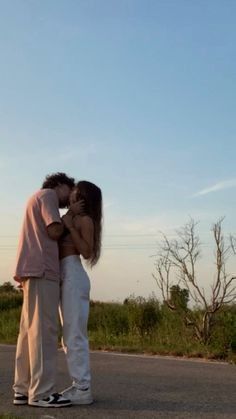 two people standing on the side of a road with their arms around each other and kissing