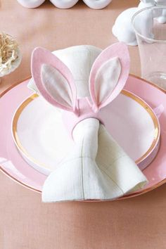 a pink table setting with napkins and bunny ears on the place settings for easter dinner