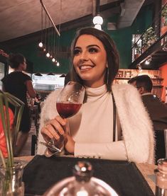 a woman sitting at a table with a glass of wine in her hand and smiling