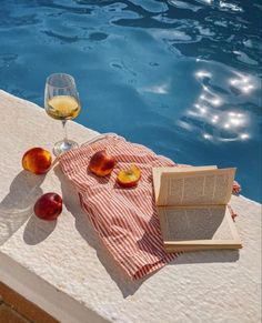 an open book sitting on top of a table next to a glass of wine and fruit