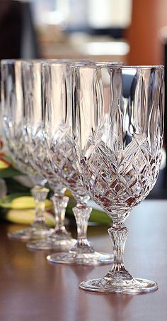 four crystal wine glasses lined up on a wooden table with flowers in the back ground