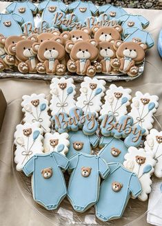 baby shower cookies are arranged on a table with teddy bears and blue onesuits