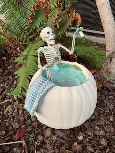 a skeleton statue sitting on top of a white pumpkin shaped bathtub in the ground