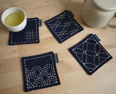 three coasters and a cup on a table with a teapot in the background