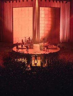 people are performing on stage in front of an audience at a concert or show with red lighting