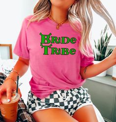 a woman sitting on a bed wearing a pink shirt with the words bride tribe printed on it