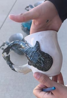 a hand holding a white and black vase with a lizard on it's side