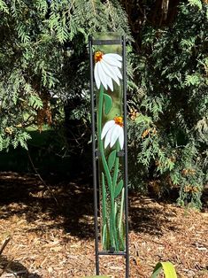 a tall metal sign with flowers painted on it's side in front of some trees