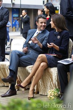 a man and woman sitting on a bench talking to each other in front of people