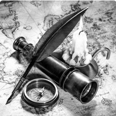 a pen, compass and ink bottle sitting on top of a map with a feather quill