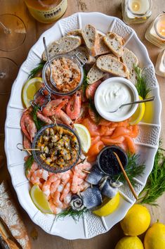 a platter filled with shrimp, bread and dipping sauces next to lemon wedges