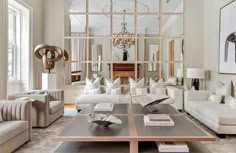 a living room filled with white couches and chairs next to a large mirror on the wall