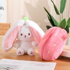 a stuffed bunny sitting next to a strawberry on a table with a book and plant