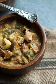 a wooden bowl filled with stew and potatoes on top of a table cloth next to a spoon