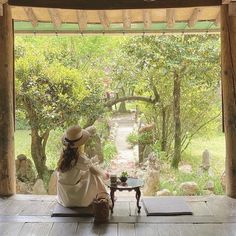 a woman sitting on top of a wooden floor in front of a stone path and trees